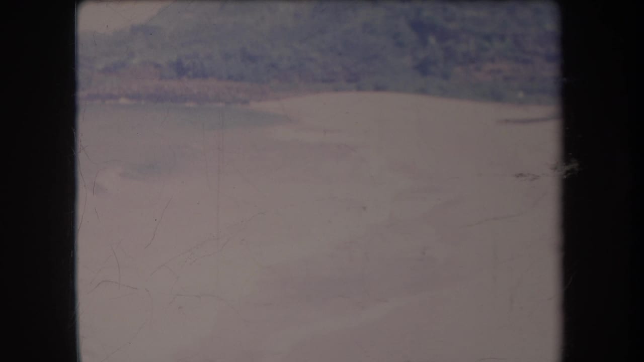 1969 Hawaii 8mm frame showing a distant shoreline, calm ocean water, and a hazy hillside in faded home-movie color.