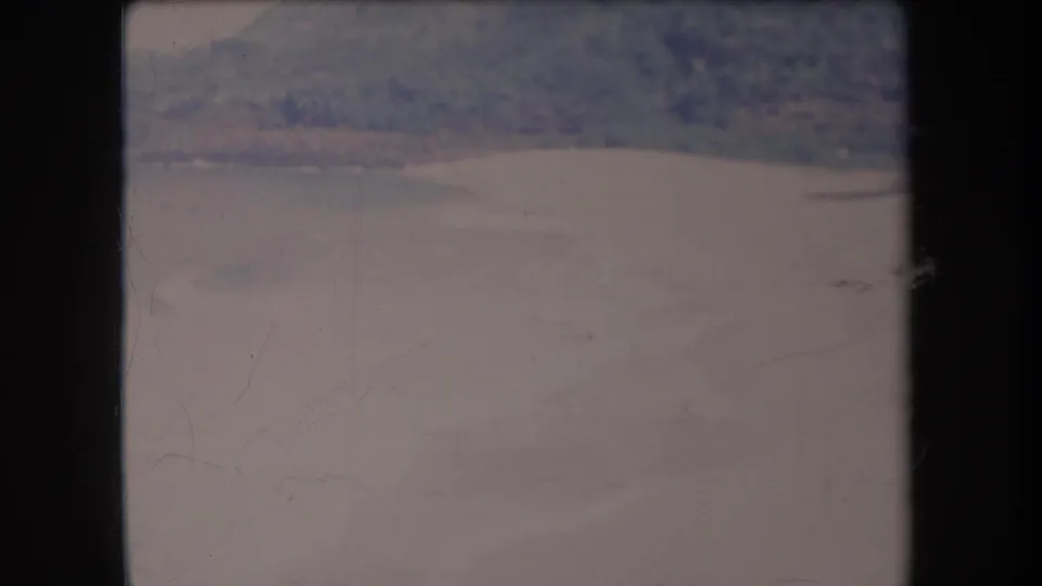 1969 Hawaii 8mm frame showing a distant shoreline, calm ocean water, and a hazy hillside in faded home-movie color.
