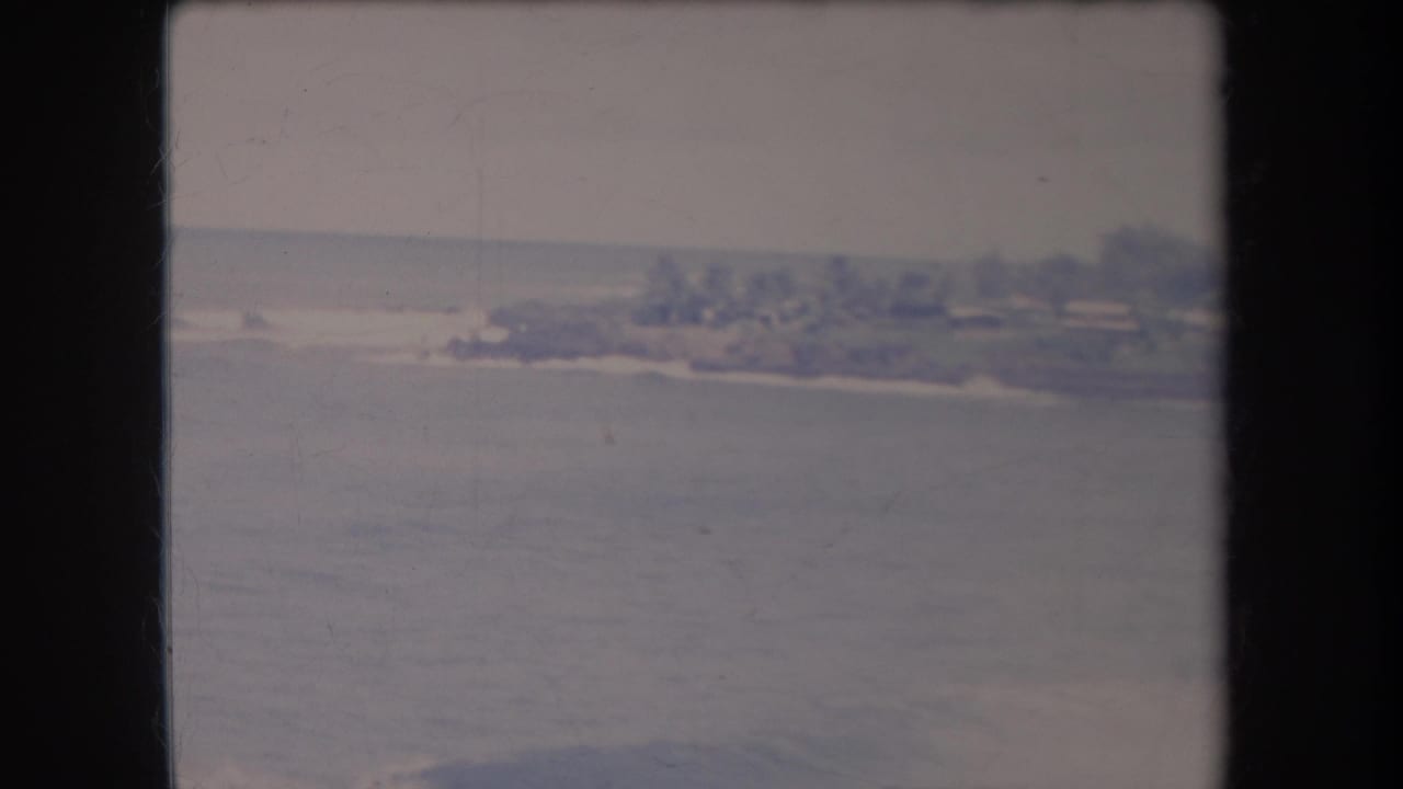 Distant shoreline across calm water beneath a pale sky, framed by dark film edges.