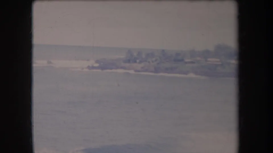 1969 Hawaii 8mm view of calm coastal water with a soft distant shoreline, low buildings, and trees under an overcast sky.