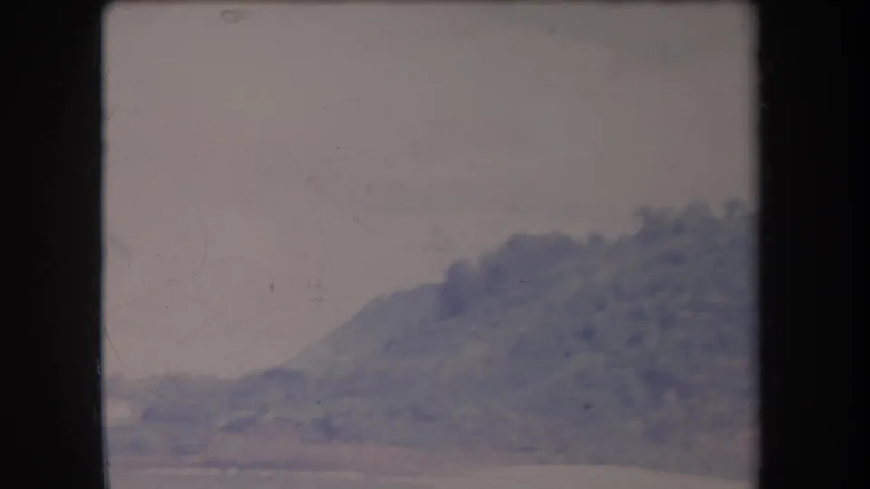 1969 Hawaii home-movie frame showing a wooded hill and shoreline in soft blue-purple color.