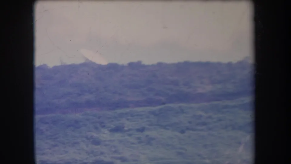 1969 Hawaii 8mm home-movie frame showing a distant foliage-covered hillside under broad daylight with soft blue-purple color shift.