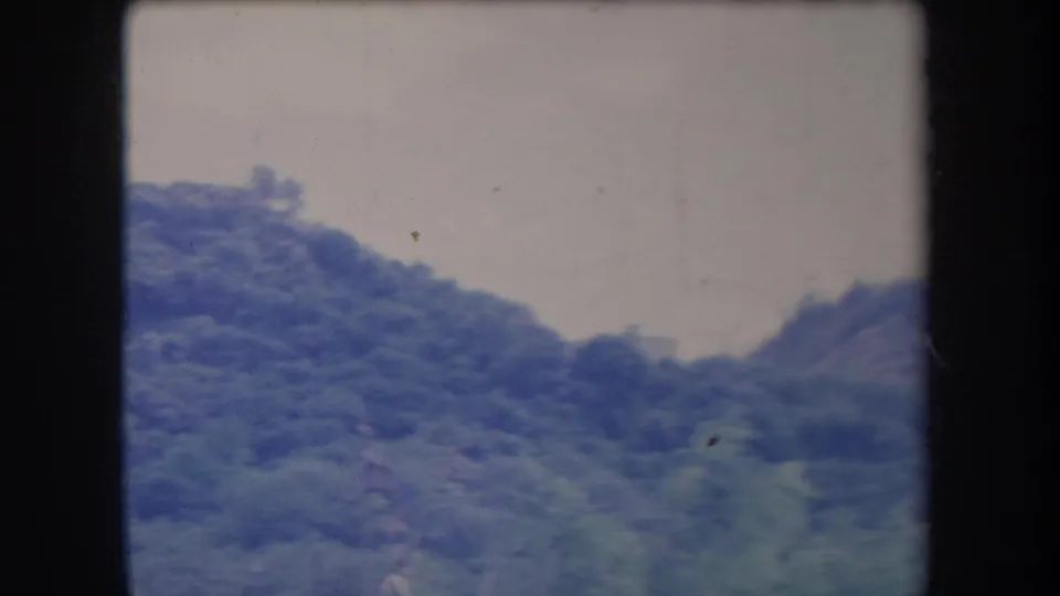 1969 Hawaii 8mm frame with layered tropical hills and leafy ridges under a bright, washed sky.