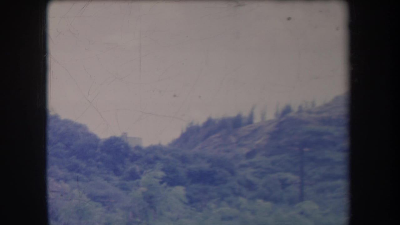 1969 Hawaii 8mm home-movie frame showing a green mountain slope and pale sky with soft focus and visible film wear.