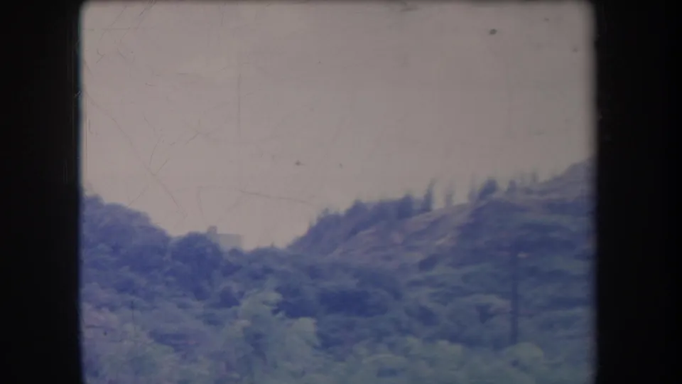 1969 Hawaii 8mm home-movie frame showing a green mountain slope and pale sky with soft focus and visible film wear.