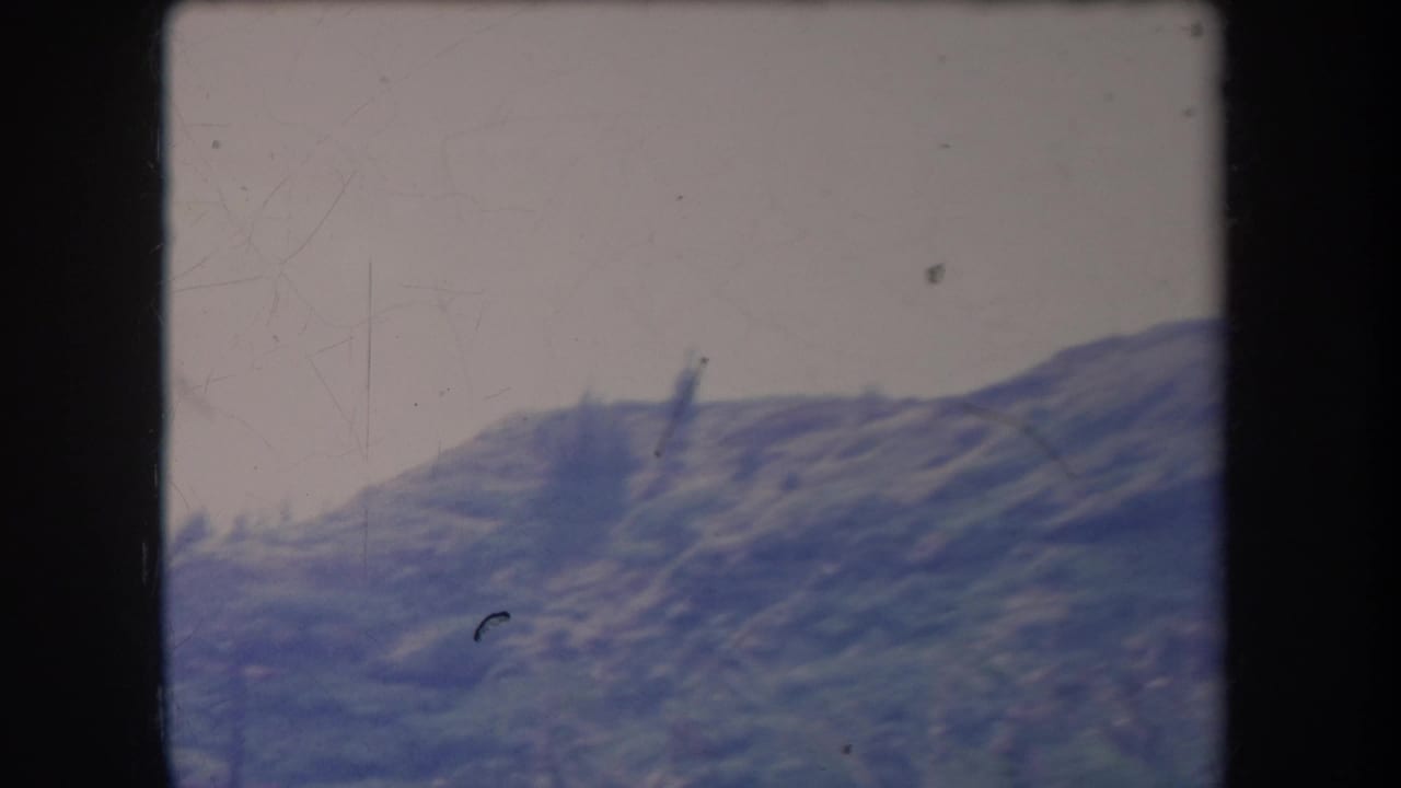 1969 Hawaii 8mm frame of a mountain range from a moving viewpoint, with faded blue-green tones and film scratches.