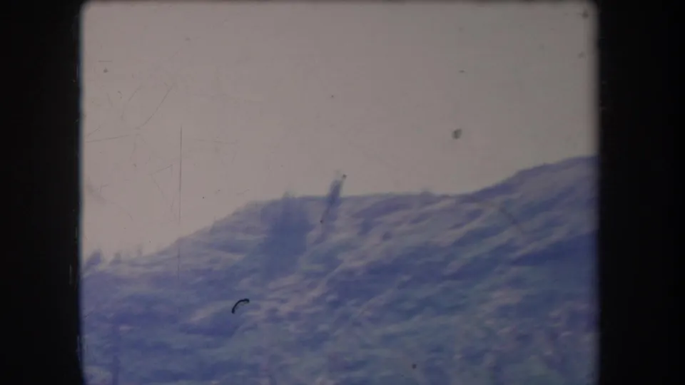 1969 Hawaii 8mm frame of a mountain range from a moving viewpoint, with faded blue-green tones and film scratches.