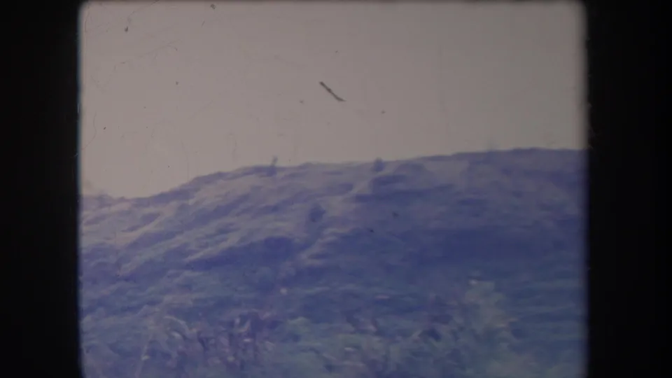1969 Hawaii 8mm home-movie view of a low green ridge under a washed pale sky, with handheld softness and surface wear.