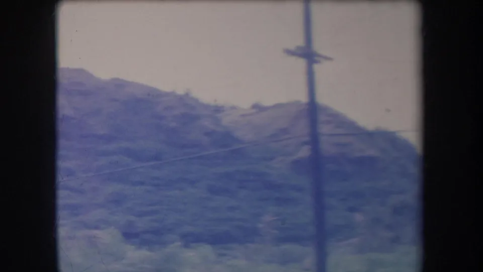 1969 Hawaii 8mm frame showing a green hillside and a roadside utility pole, filmed from a moving vehicle.