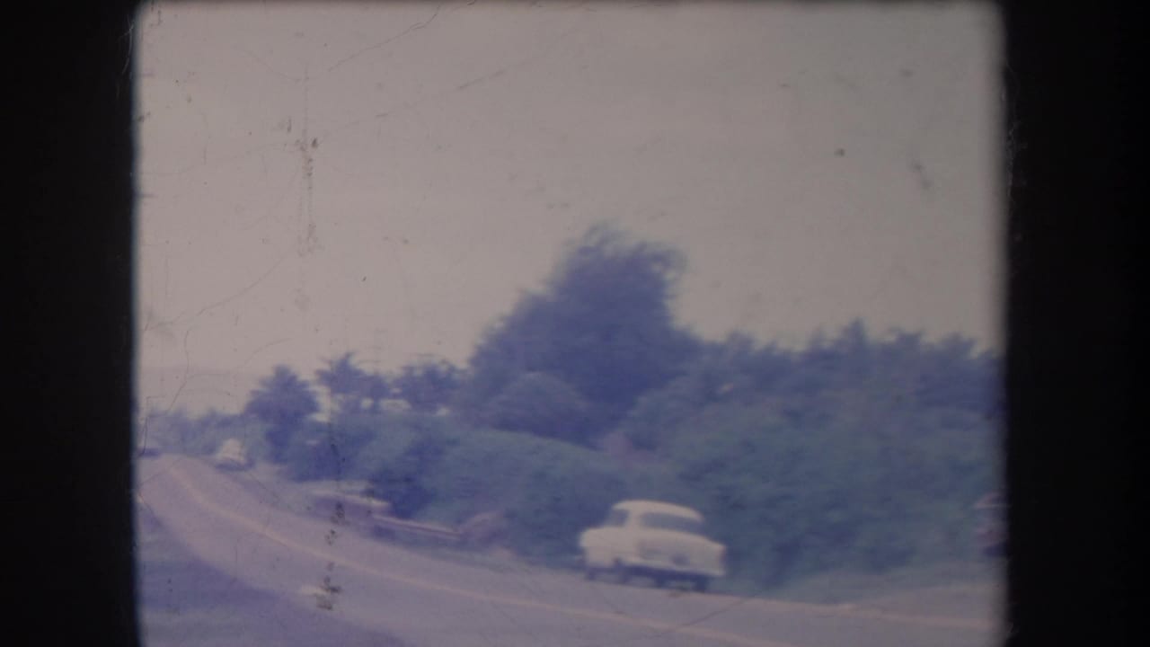 Soft 8mm frame from 1969 Hawaii showing a winding roadside bordered by dense vegetation and a white period car.