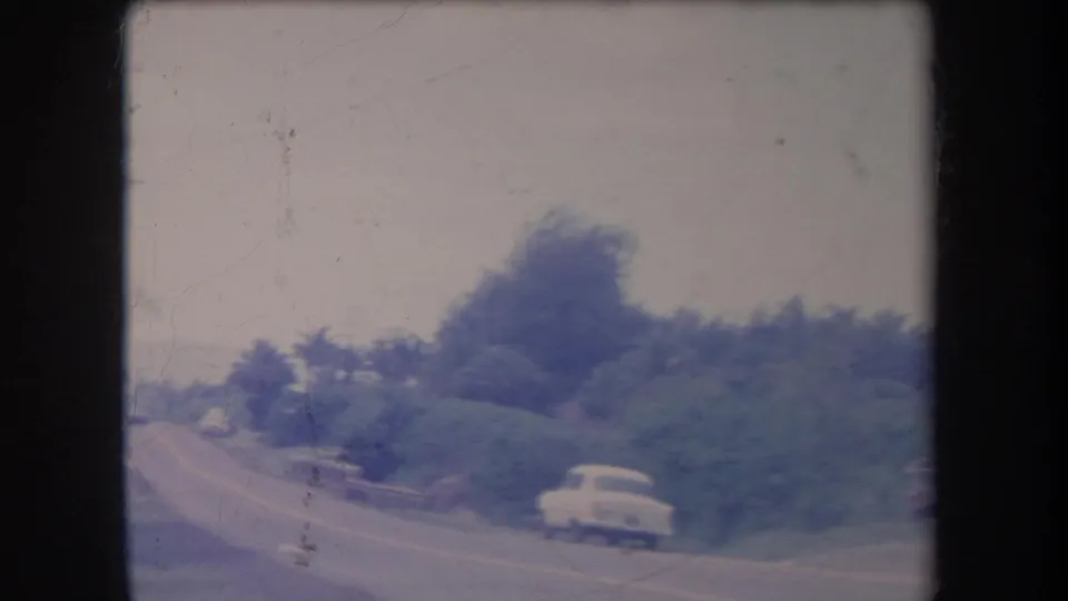 Soft 8mm frame from 1969 Hawaii showing a winding roadside bordered by dense vegetation and a white period car.