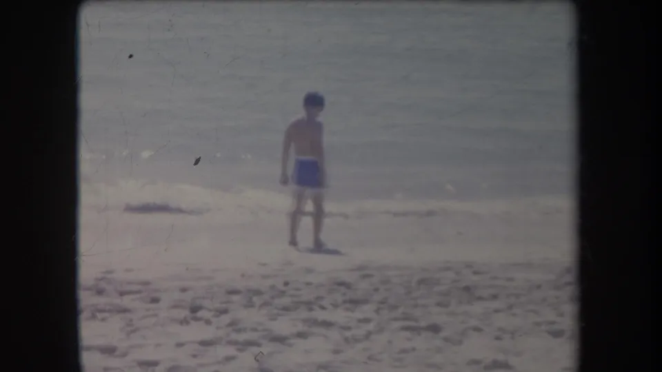 1969 Hawaii beach frame showing a boy from behind near the surf, with soft focus, grain, and faded color.