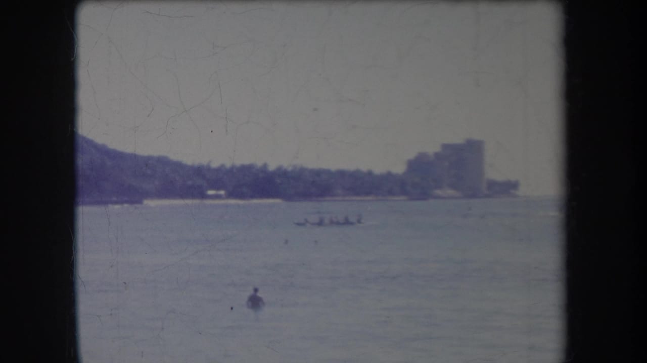 Distant shoreline and building across calm water with small boats and a swimmer visible.