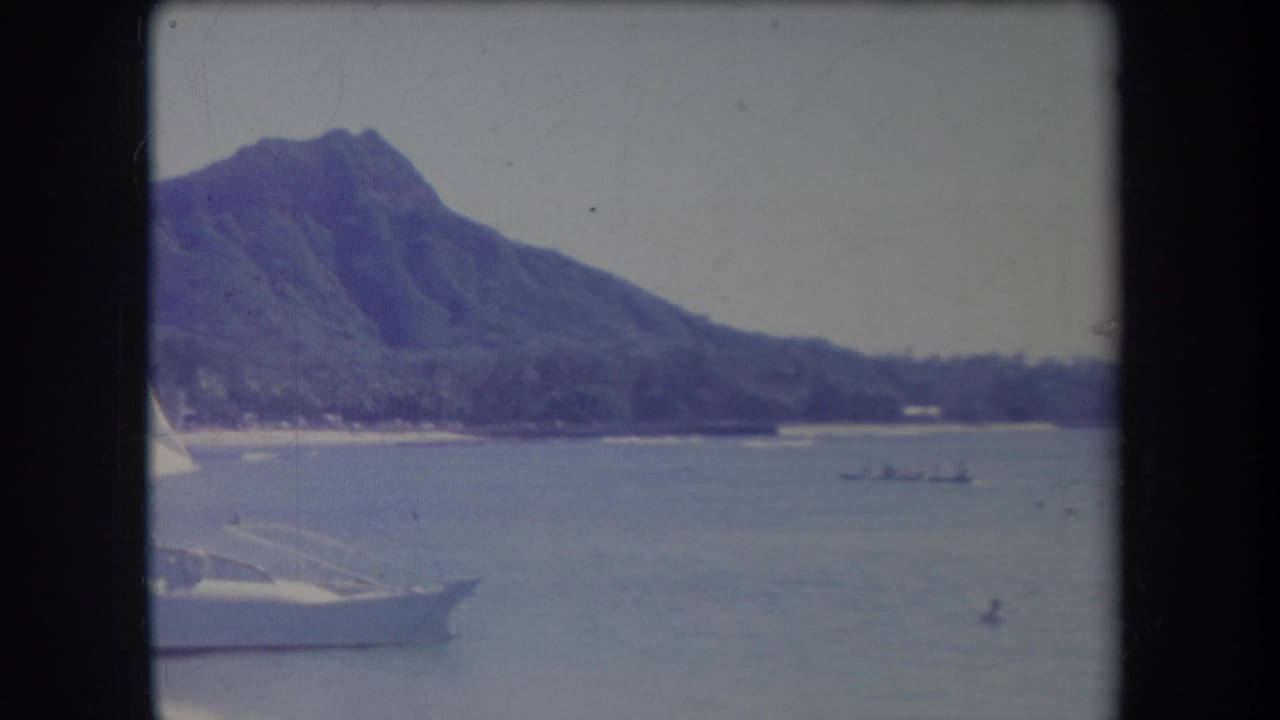 1969 Hawaii home-movie view of Diamond Head across the water, with a small boat offshore and part of a white sailboat entering the frame.