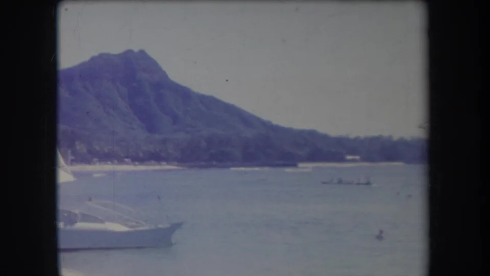 1969 Hawaii home-movie view of Diamond Head across the water, with a small boat offshore and part of a white sailboat entering the frame.