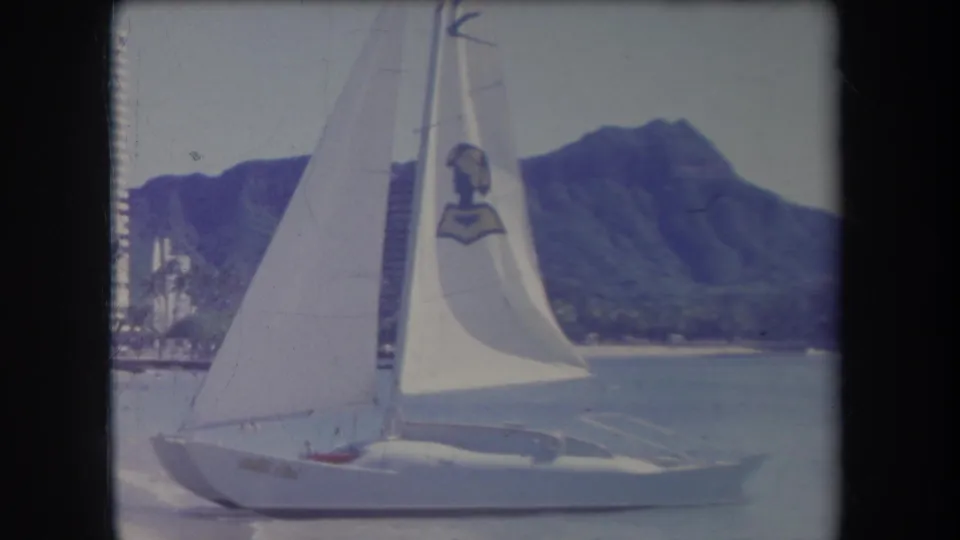 The sailboat fills much of the foreground near the beach, with Diamond Head and shoreline development visible in the background.