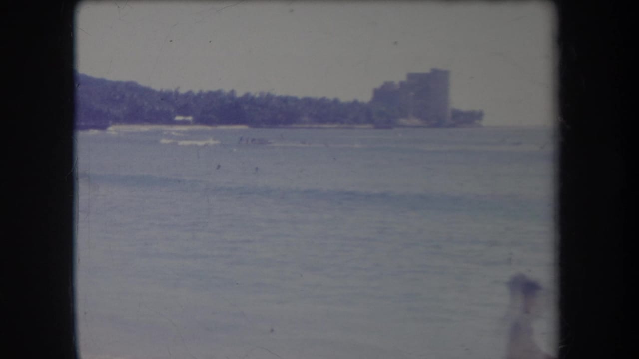 A beachgoer stands near the right edge as small boats appear on calm water offshore.