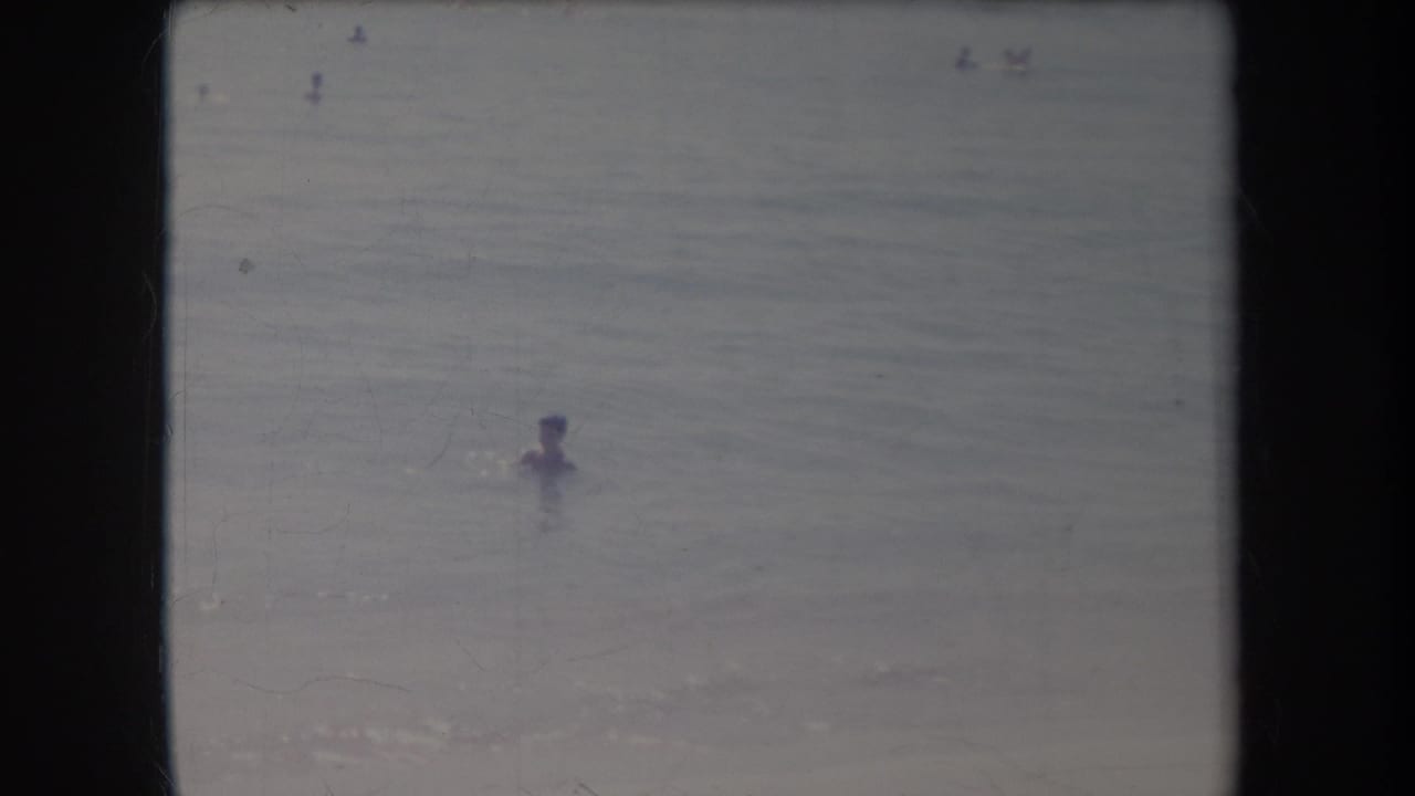 Swimmer floating in the ocean with faint figures farther out.
