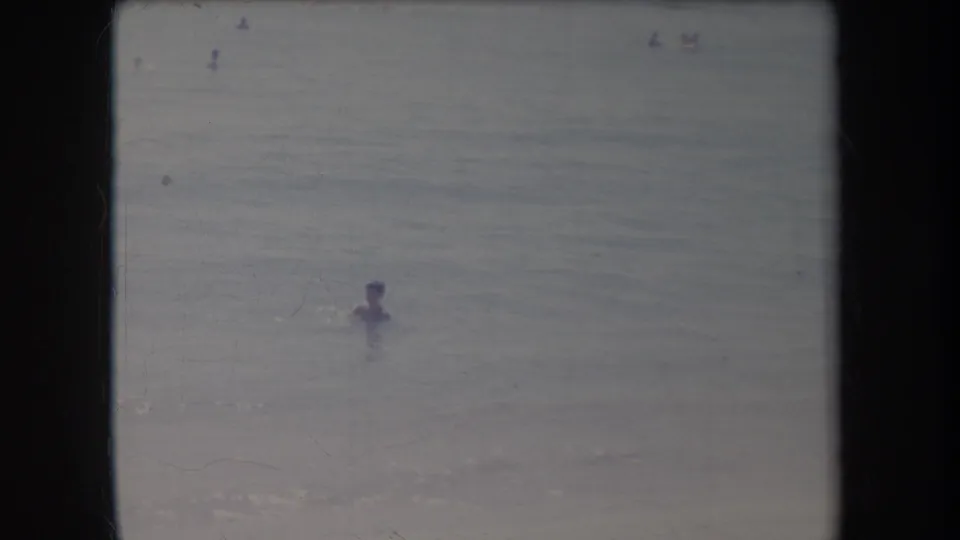 1969 Hawaii beach frame with a swimmer in the water and indistinct figures in the distance.