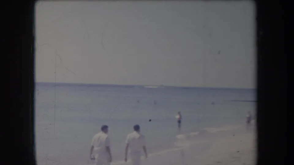 The men in white recede along a Hawaii beach in 1969, with swimmers and beachgoers spaced across the surf and sand.