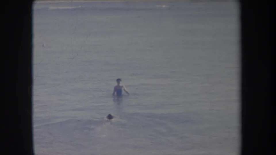 1969 Hawaii beach footage shows a standing bather in shallow water and a smaller swimmer partly submerged closer to the camera.