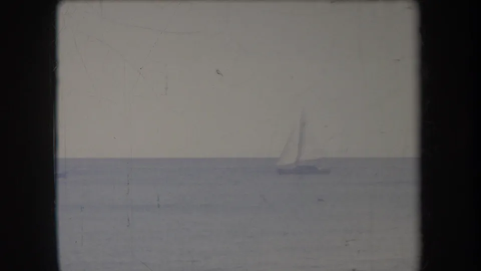 Distant sailboat on calm Hawaii ocean water in a faded 1969 8mm home-movie frame with soft grain and visible frame border.
