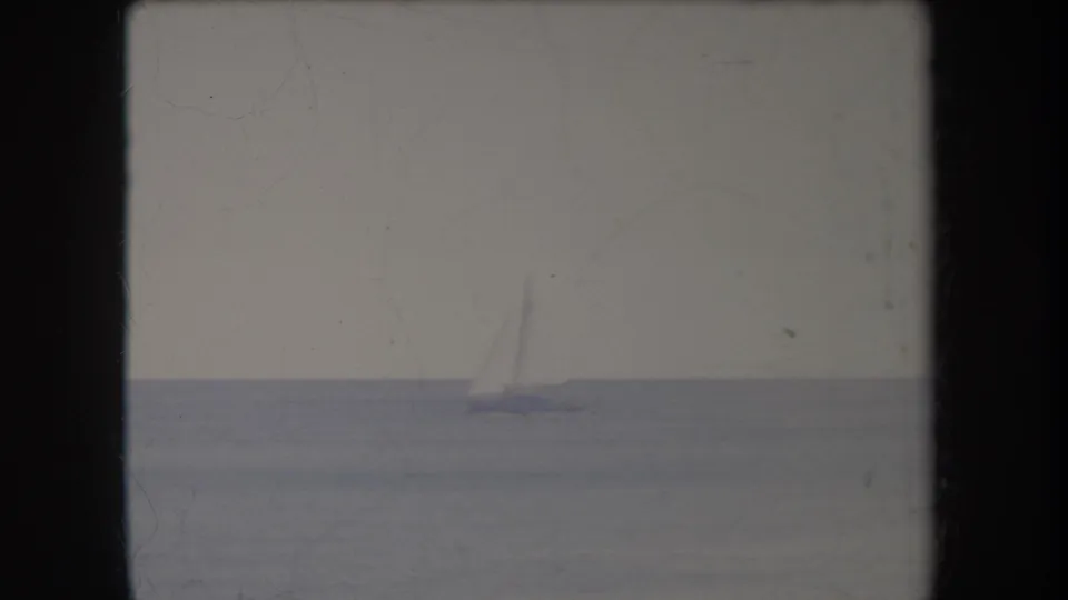 A faint distant sailboat sits low against the calm Hawaii waterline in a scratched, faded 1969 8mm frame.