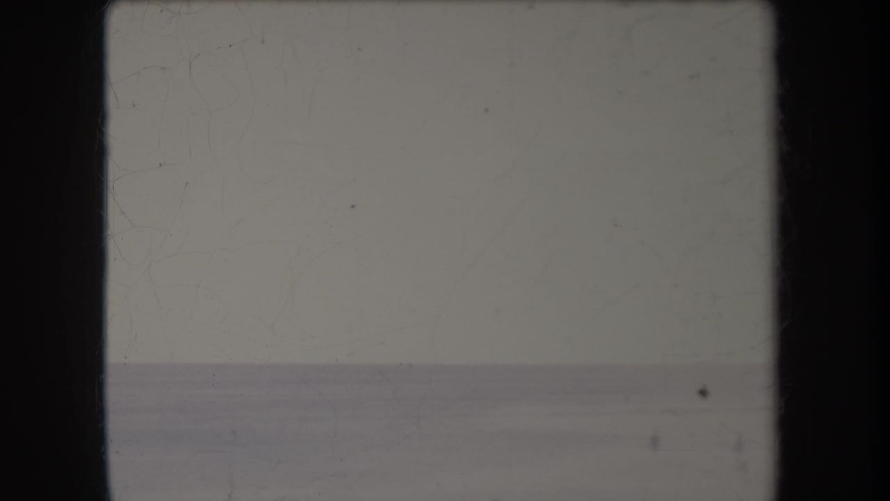 Faded ocean horizon under pale sky with film gate edges and surface wear.