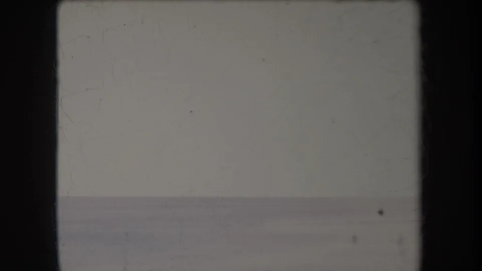 1969 Hawaii 8mm frame showing a calm ocean horizon beneath a pale sky, with visible dust, scratches, and dark film borders.