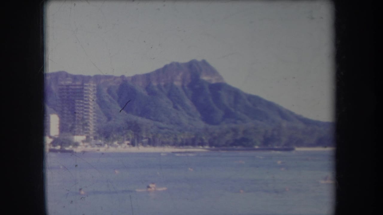 1969 Hawaii 8mm frame showing Diamond Head beyond blue water, distant swimmers, and shoreline high-rises at the edge of the beach.