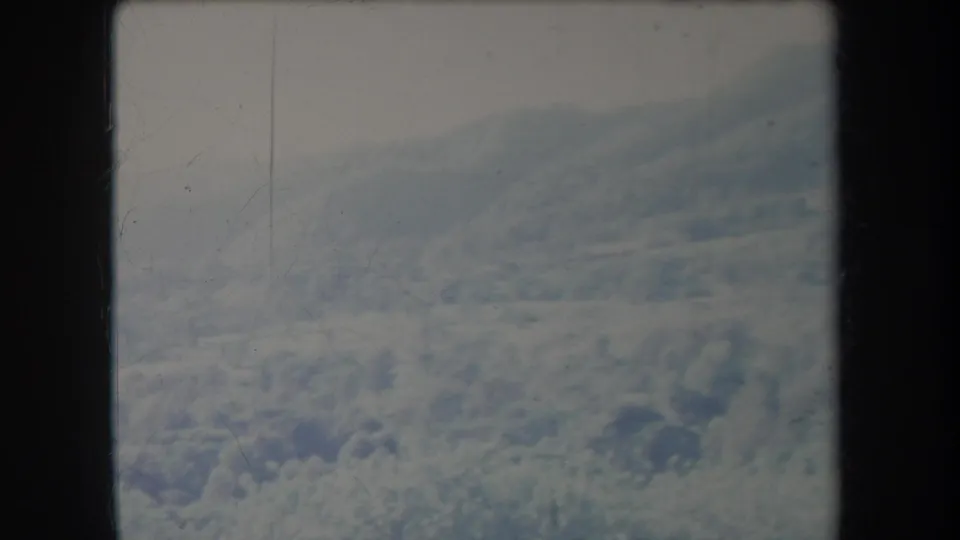 1969 home-movie aerial view of cloud banks and a broad snow-covered mountain slope, with muted color and visible film wear.