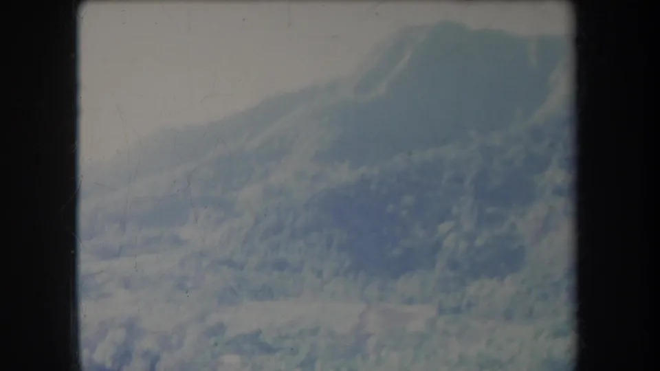 1969 Hawaii home-movie frame of a vegetated mountain slope and small peak in soft overcast light.