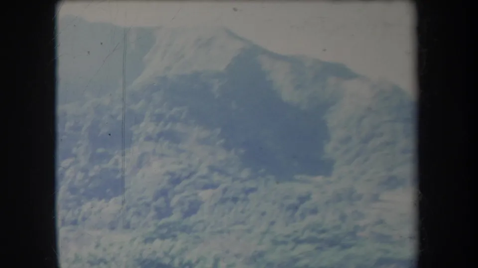1969 Hawaii home-movie frame showing a rocky, shrub-covered slope with a darker recessed area.