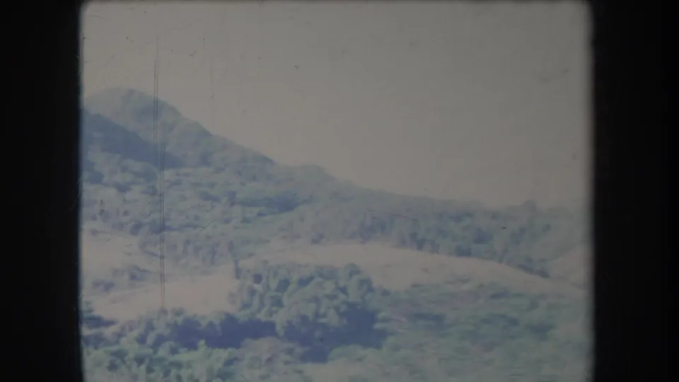 1969 Hawaii home-movie frame with distant forested ridges, low vegetation, washed color, and visible 8mm gate borders.