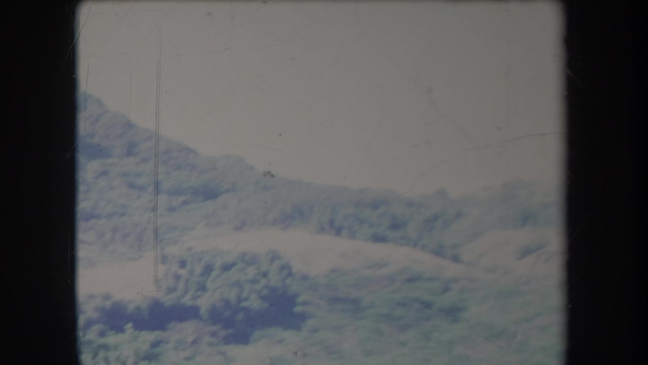 1969 Hawaii 8mm frame showing rolling pasture and hazy mountain slopes under a pale cloudy sky.