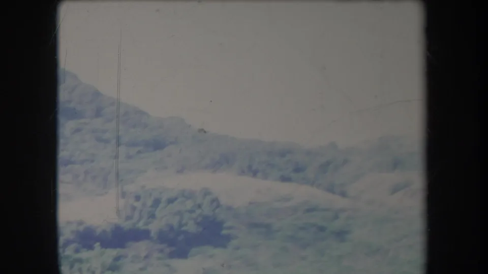 1969 Hawaii 8mm frame showing rolling pasture and hazy mountain slopes under a pale cloudy sky.