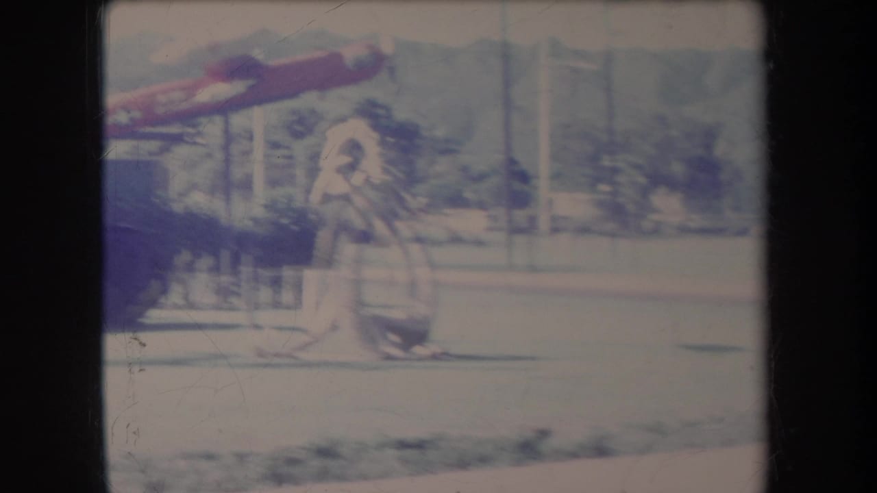 1969 Hawaii home-movie frame showing a red aircraft model above a white figure sculpture in a park-like military display.