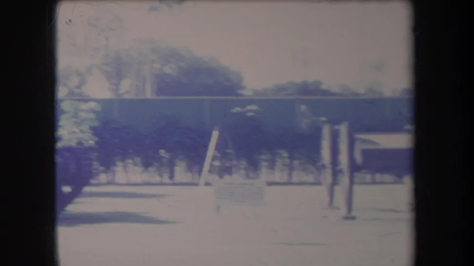 1969 Hawaii home-movie frame with fencing, lawn, posts, and trees as the camera pans across the exhibit grounds.