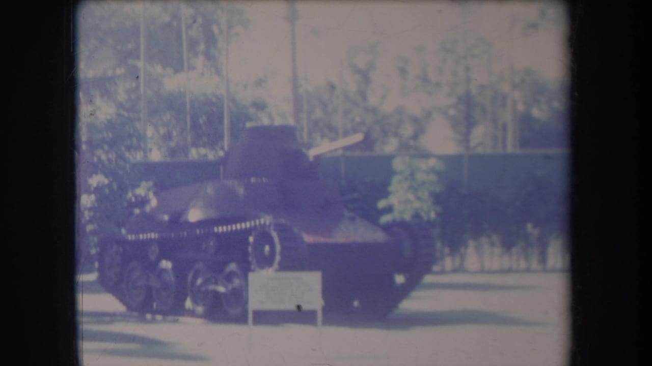 1969 Hawaii home-movie frame showing a small military tank on outdoor display beside a white sign and tropical foliage.