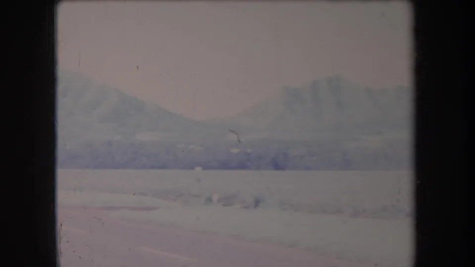 1969 Hawaii home-movie frame showing a road edge, low foreground wall or curb, and distant mountains in haze.