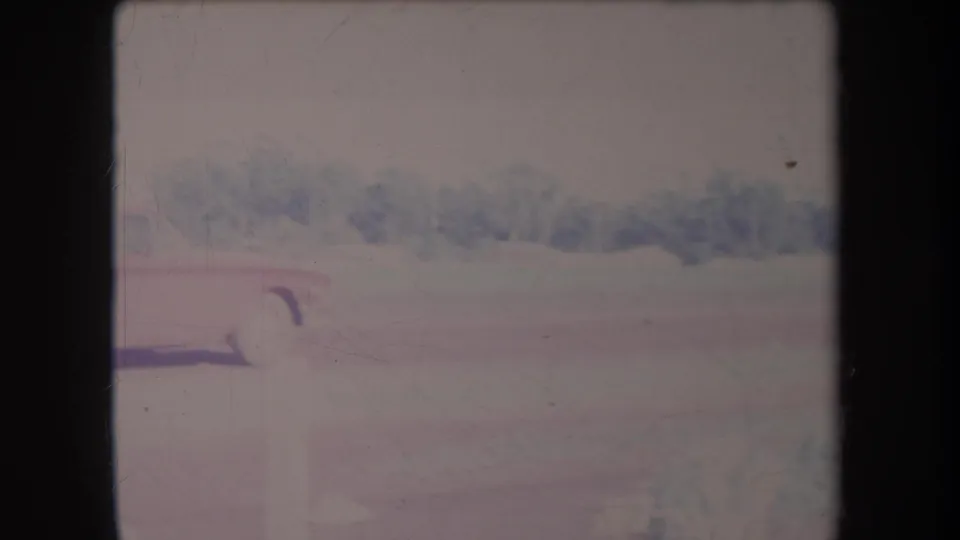 1969 Hawaii home-movie frame with part of a red sedan visible against a pale driveway and distant tree line.