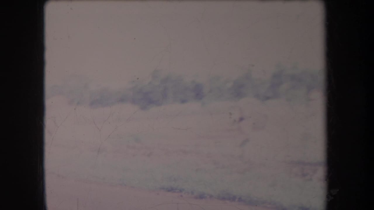 Hazy mountain landscape with pale sky, soft focus, dust, scratches, and dark film borders.