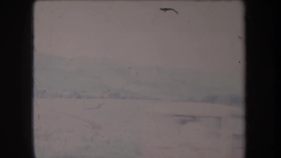 1969 Hawaii 8mm frame showing faint hills and roadside terrain in soft haze, with scratches and faded pink-blue color.