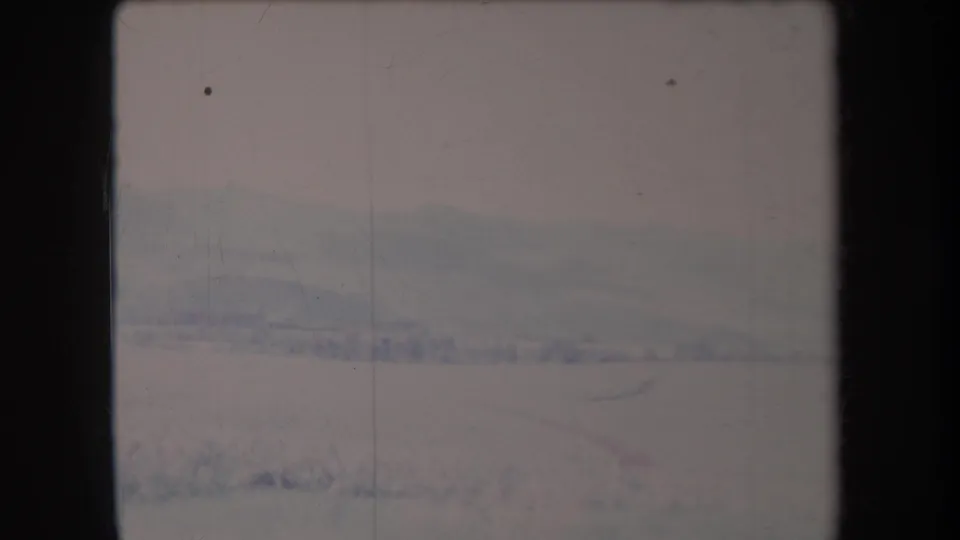 1969 Hawaii home-movie frame of distant mountains and open land beneath a cloudy sky, rendered in faded 8mm color.