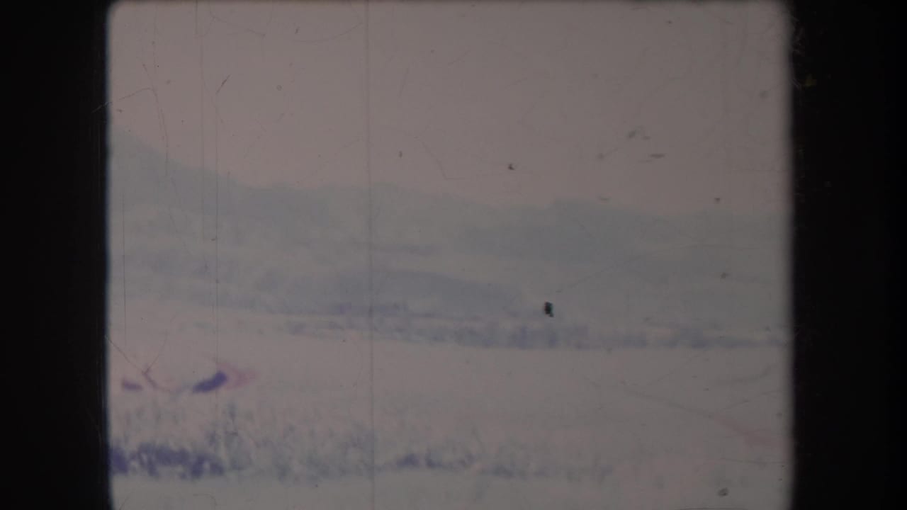 Faded 8mm frame of a hazy field with distant mountains and dark film borders.