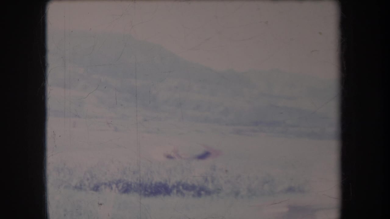 Hazy mountain landscape with grass and a small dark moving speck in the frame.