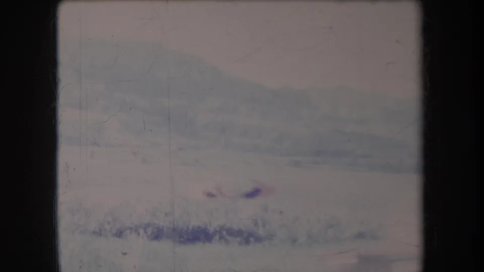 1969 Hawaii 8mm frame of a hazy field and distant ridge, with a small indistinct object crossing quickly.