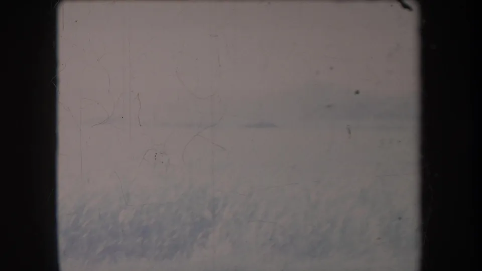 1969 Hawaii 8mm frame showing a pale open field, faint horizon line, lower grass, dust marks, and scratched film texture.