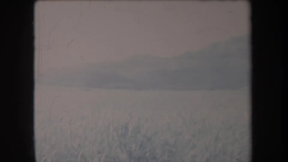 1969 Hawaii 8mm frame with a subdued hillside and grassy valley seen through scratched film.