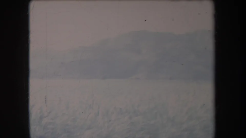 1969 Hawaii home-movie frame showing a quiet grassy valley and distant rounded hills in haze.